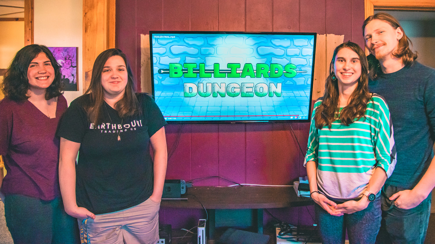 From left, marketer Sheila Johnson, artist Calista Brasher, marketing manager Catherine Cleveland and game designer William Cleveland smile for a photo in front of the logo for their company’s new game, “Billiards Dungeon,” which will be released on July 30.